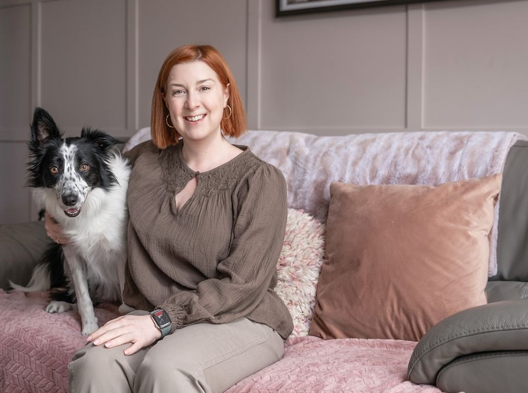 About Dr Karen Lumsden - white woman with strawberry blonde hair, wearing greeny-blue top, sitting at a kitchen table with a blue mug in her hands.